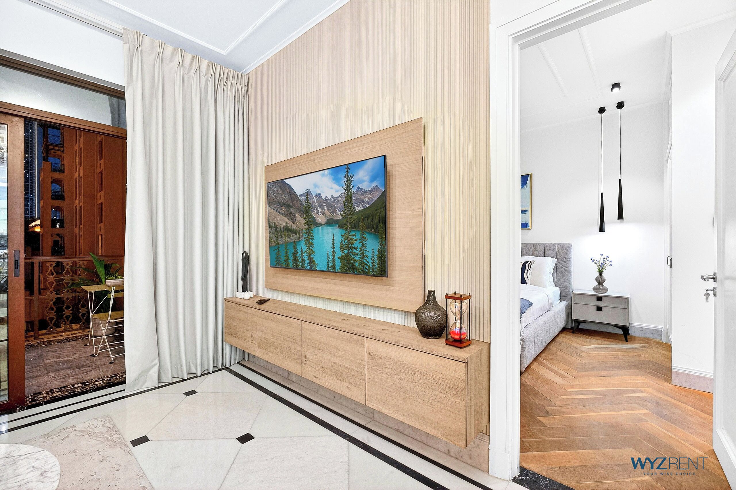 A modern hotel room with a wooden console, a large framed picture, a bed, and a nightstand with a lamp.