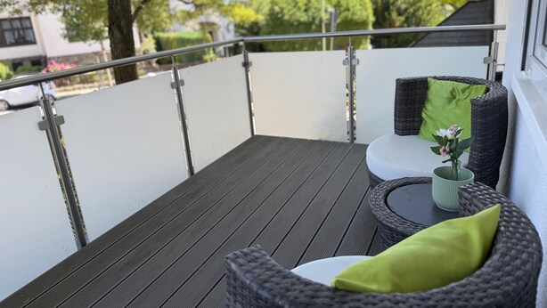 A balcony with a wicker sofa, a small table, and a potted plant.