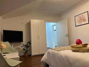 Makuuhuoneessa on sänky, televisio, vaatekaappi ja ovi, joka johtaa toiseen huoneeseen.