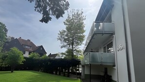 A modern building with a balcony, a well-maintained lawn, and a clear sky.
