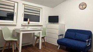 A small room with a white table, two chairs, a blue sofa, a TV, and a clock on the wall.