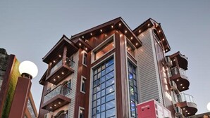 A modern multi-story building with a prominent central glass facade, multiple balconies, and a series of lights along the roofline. - Hotel Aura Inn (Srinagar)