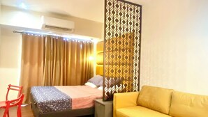 A room with a bed, a yellow sofa, a red chair, a decorative partition, and a ceiling fan. - Opulent Studio in delightful Makati with fantastic Amenities (Makati)