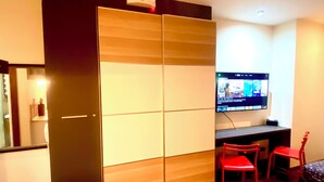 A room with a sliding wardrobe, a flat-screen TV mounted on the wall, and two red chairs. - Opulent Studio in delightful Makati with fantastic Amenities (Makati)