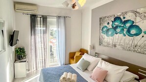 Een hotelkamer met een bed, een schilderij, een plant en een raam met gordijnen.