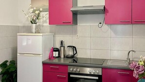 Een keuken met roze kastjes, een witte koelkast, een fornuis en een spoelbak.