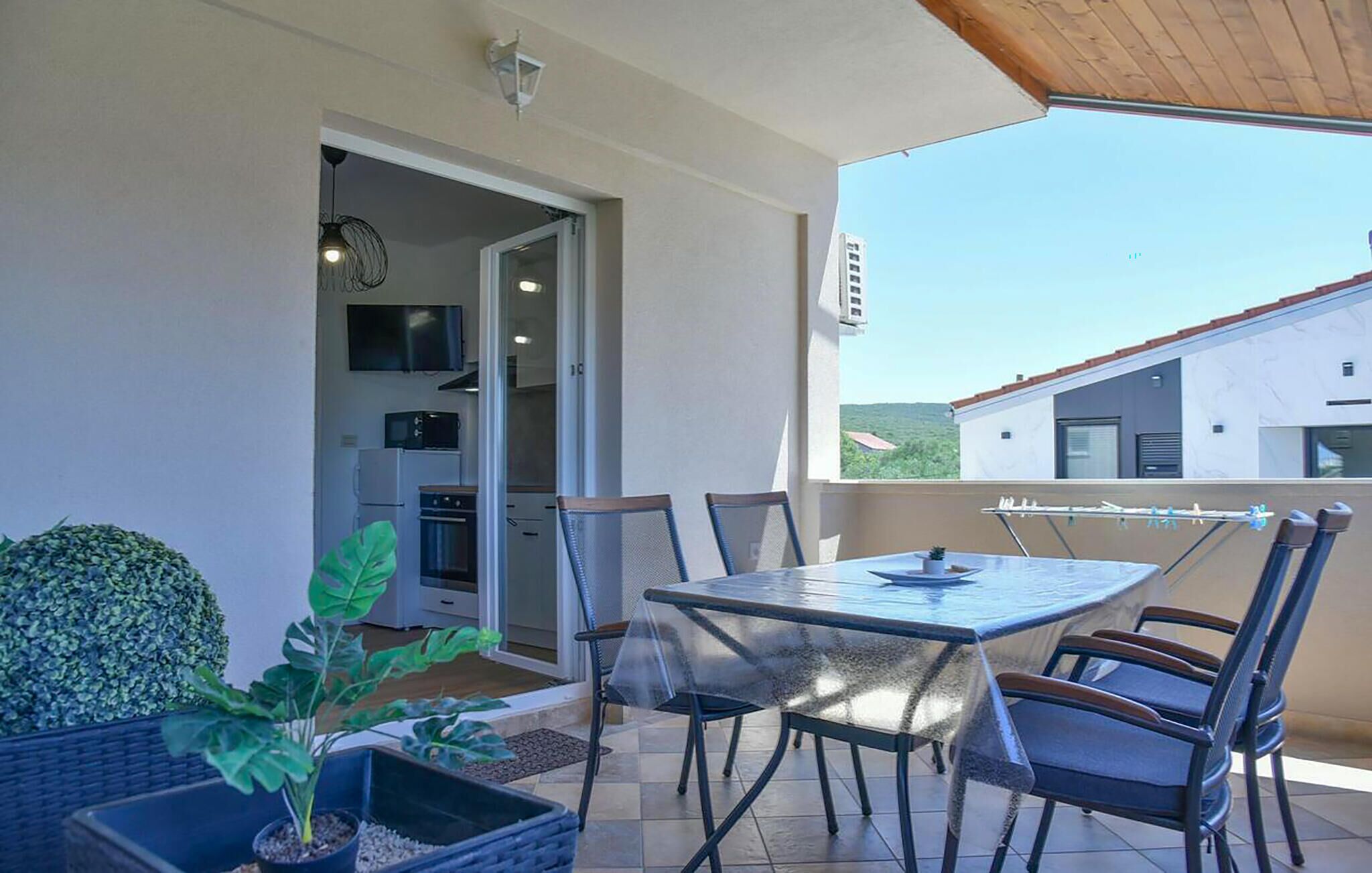 A balcony with a table and chairs, a potted plant, and a view of a building and landscape.