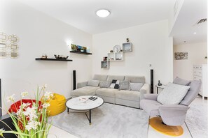 Un salon moderne avec un canapé d’angle gris, un fauteuil poire rouge, une table basse blanche et un fauteuil à accoudoirs gris.