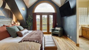A bedroom with a large bed, a bench, a chair, a TV mounted on the wall, and a view through a large window. - Skate Bowl, Climbing Wall, Arcade | Breckenridge Adventure Chalet by AvantStay (Breckenridge)