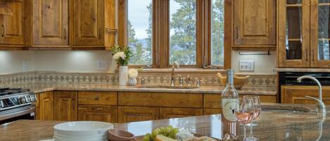 A kitchen with wooden cabinets, a granite countertop, a window with a view, and a wine bottle and glasses on the counter.