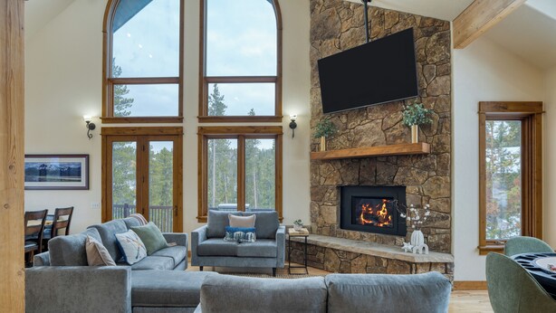 Amplia sala de estar con chimenea de piedra, ventanas grandes y televisor de pantalla plana montado en la pared.