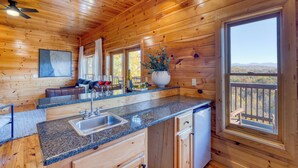 Interior de una cabaña de madera con cocina, una mesa de comedor y un amplio ventanal con vistas panorámicas.
