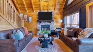 Un acogedor interior de cabaña de madera con chimenea de piedra, sofás de cuero y un televisor de pantalla plana grande.
