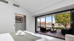 Quarto moderno com cama grande, vista para o exterior e área de estar com sofá e cadeiras.