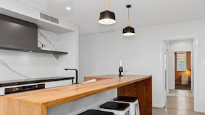 Uma cozinha moderna com painel de mármore, balcão de madeira e banquetas pretas.