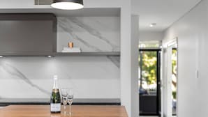 Uma cozinha moderna com painel de fundo de mármore, uma mesa de madeira com uma garrafa de champanhe e duas taças, e vista para um jardim por uma porta aberta.