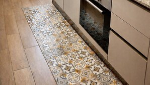 Eine kompakte Küche mit Gasherd, Backofen und Spüle. Ein Esstisch mit Blumen in einer Vase und einer Uhr an der Wand.