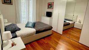 Ein modernes Schlafzimmer mit Bett, Nachttisch, Lampe und einem großen Spiegel.