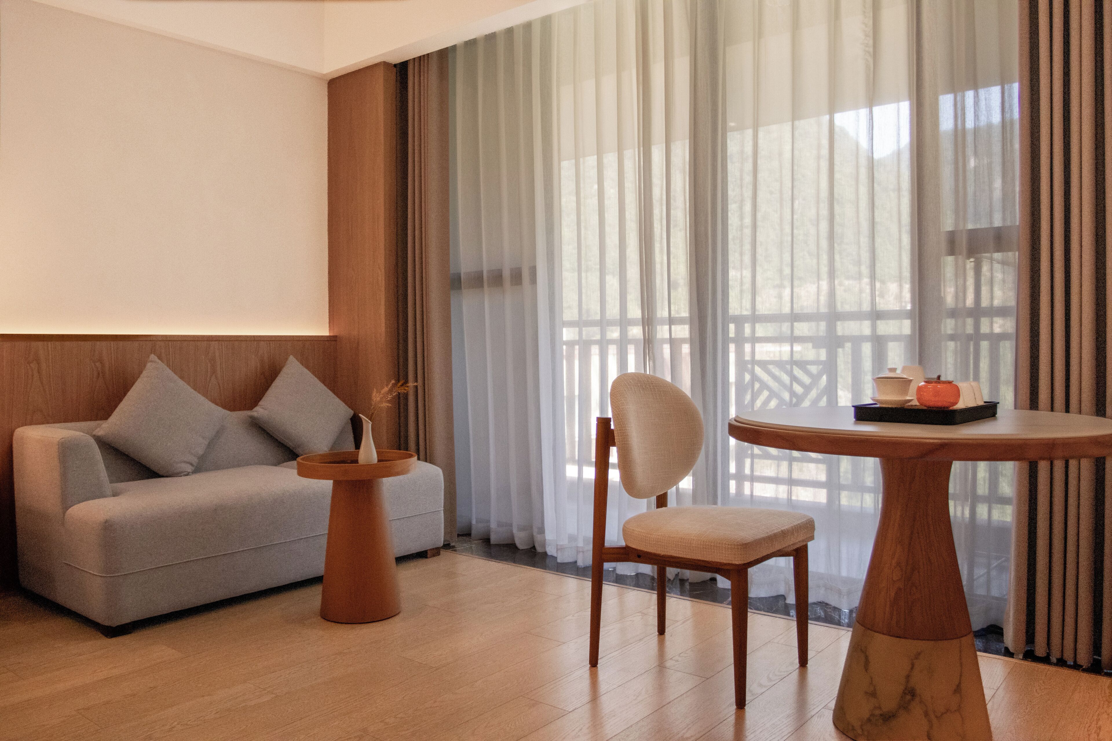 Una habitación moderna con un sofá, una silla, una mesa redonda y vistas a través de cortinas translúcidas.