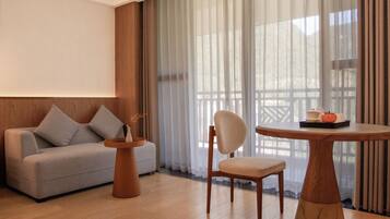 Una habitación moderna con un sofá, una silla, una mesa redonda y vistas a través de cortinas translúcidas.