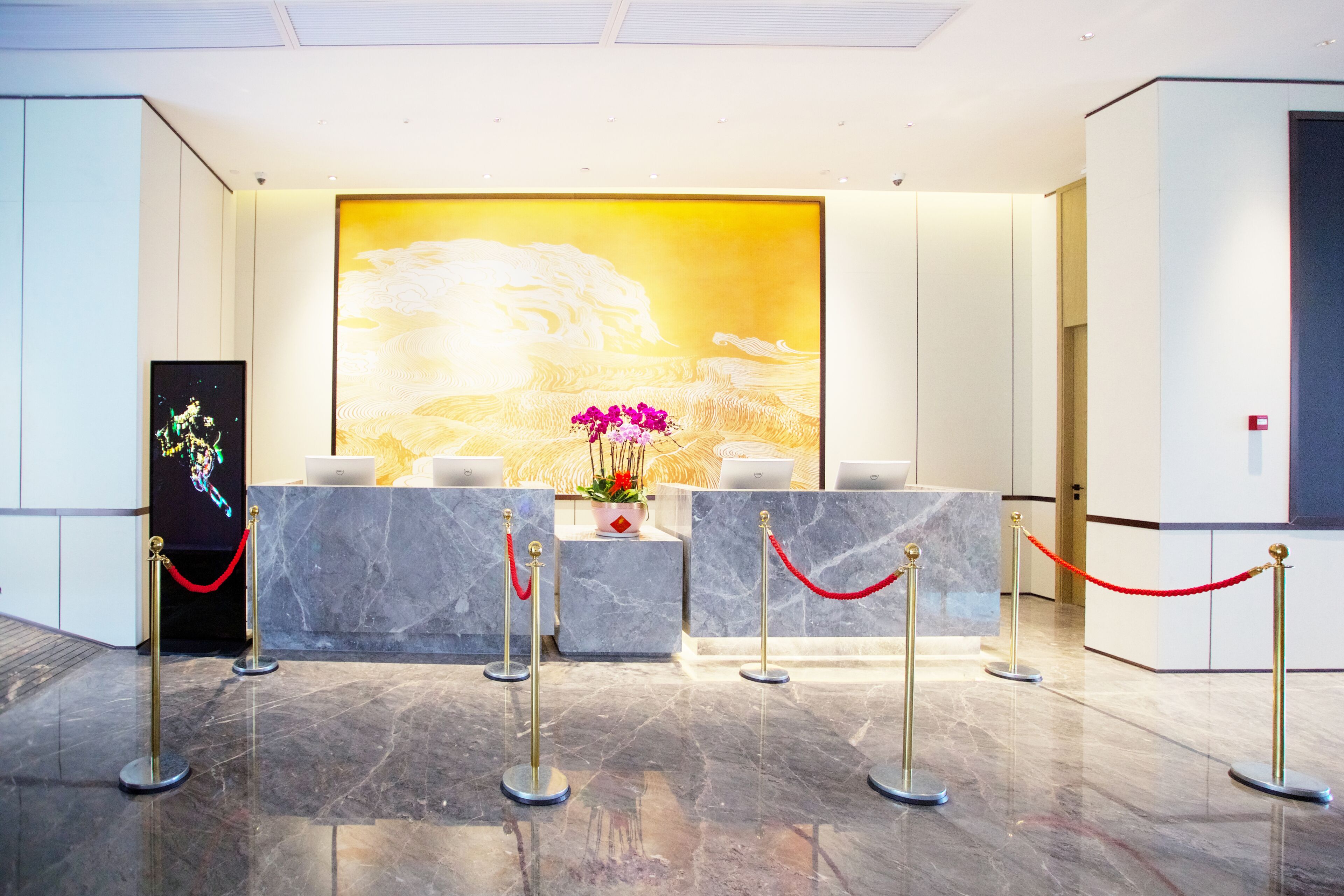 A reception area with a marble counter, a large wall mural, and a red rope barrier.