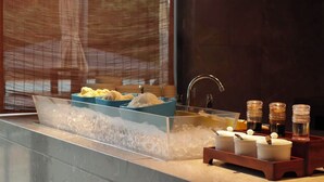 A modern bathroom with a glass bathtub filled with ice, a sink with a faucet, and a tray with toiletries. - Fuzhou Royal Hot Spring Hotel & Resort (Fuzhou)