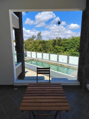 Ein Zimmer mit Blick auf einen Swimmingpool, einer hölzernen Bank und einer Glastür zum Außenbereich.