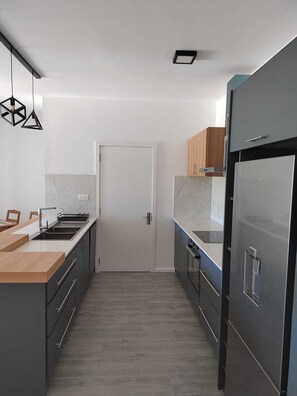 Eine moderne Küche mit grauen Schränken, einem Edelstahl-Kühlschrank und einer Holz Arbeitsplatte.