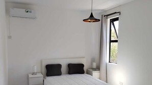 Een moderne slaapkamer met een bed, twee nachtkastjes, een hanglamp, een raam en een airconditioner.