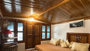Une chambre avec un plafond en bois, un lit recouvert de plusieurs oreillers, une lampe rouge et un tableau encadré accroché au mur.
