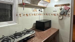 Une cuisine avec des meubles de rangement en bois, une cuisinière à gaz, un four à micro-ondes et une fenêtre.