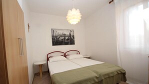 A bedroom with a bed, a bedside table, a hanging light fixture, a painting on the wall, and a window with curtains. - Welcoming apartment steps from the beach (Rosolina Mare)
