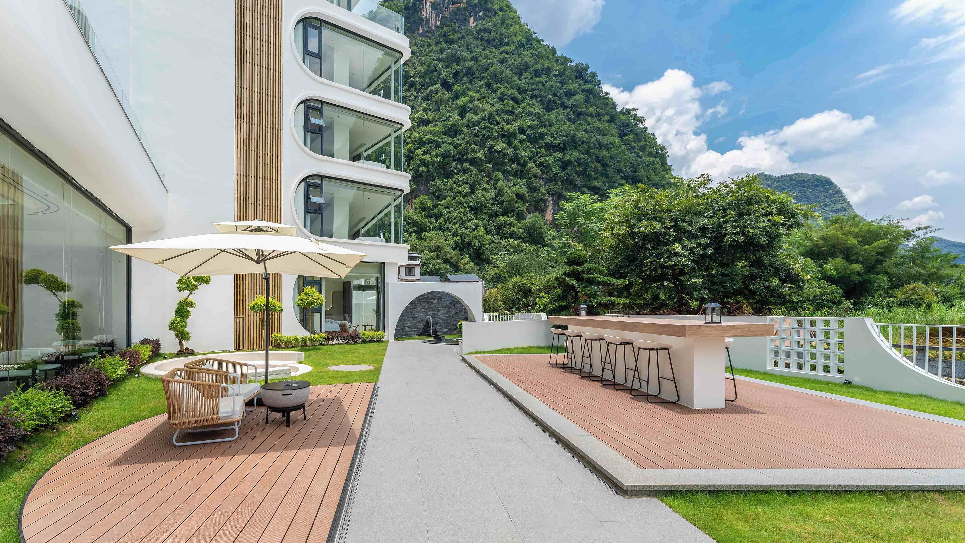 Un hotel moderno con estructura de varios niveles, zona de estar al aire libre y vistas a una exuberante montaña verde.