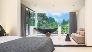 A modern hotel room with a large bed, a sofa, a black bathtub, and a view of lush greenery. - Karst Scenic Hotel (Guilin)