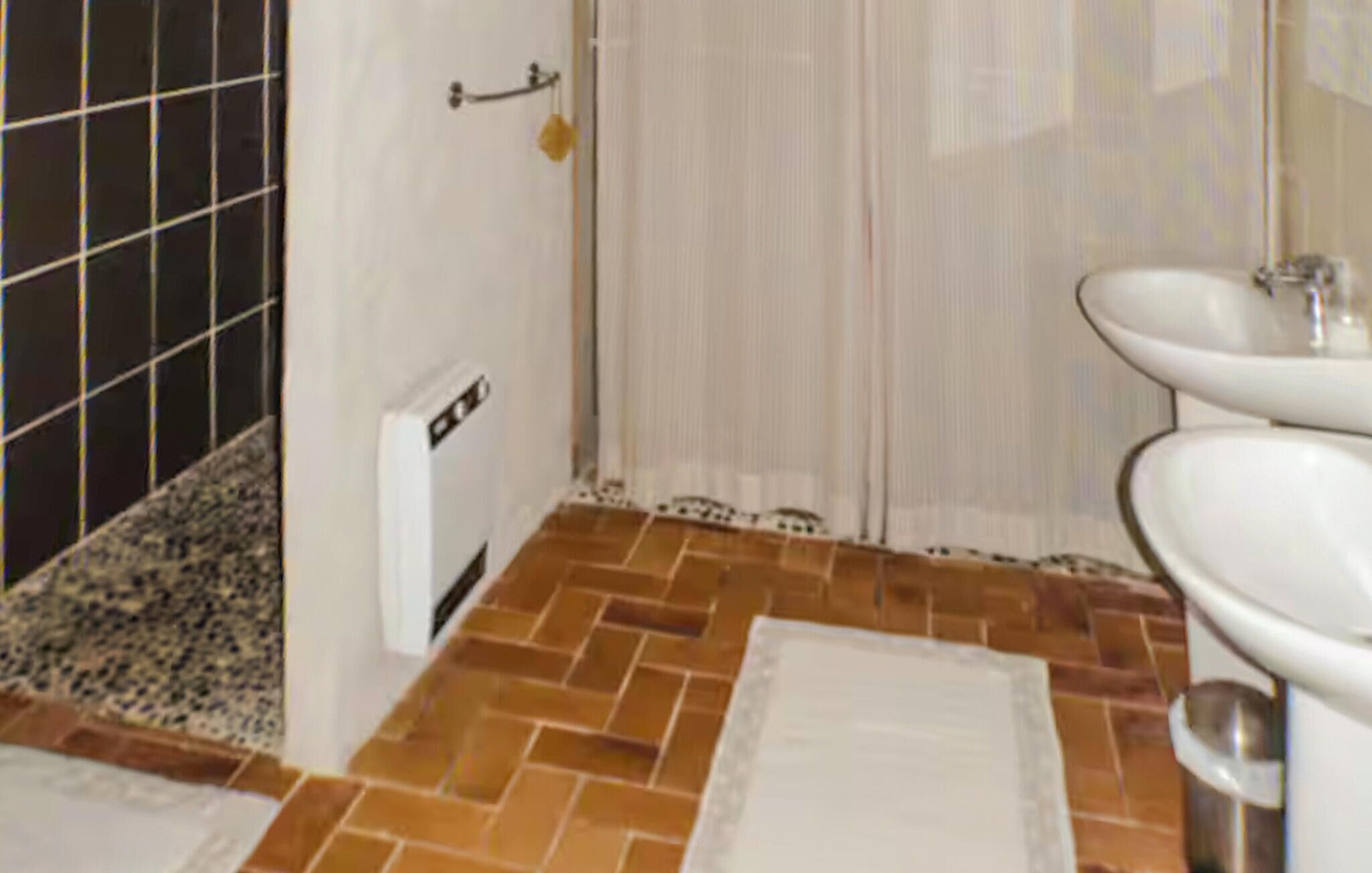 A bathroom with a white sink, a mirror, and a shower area with a tiled floor.