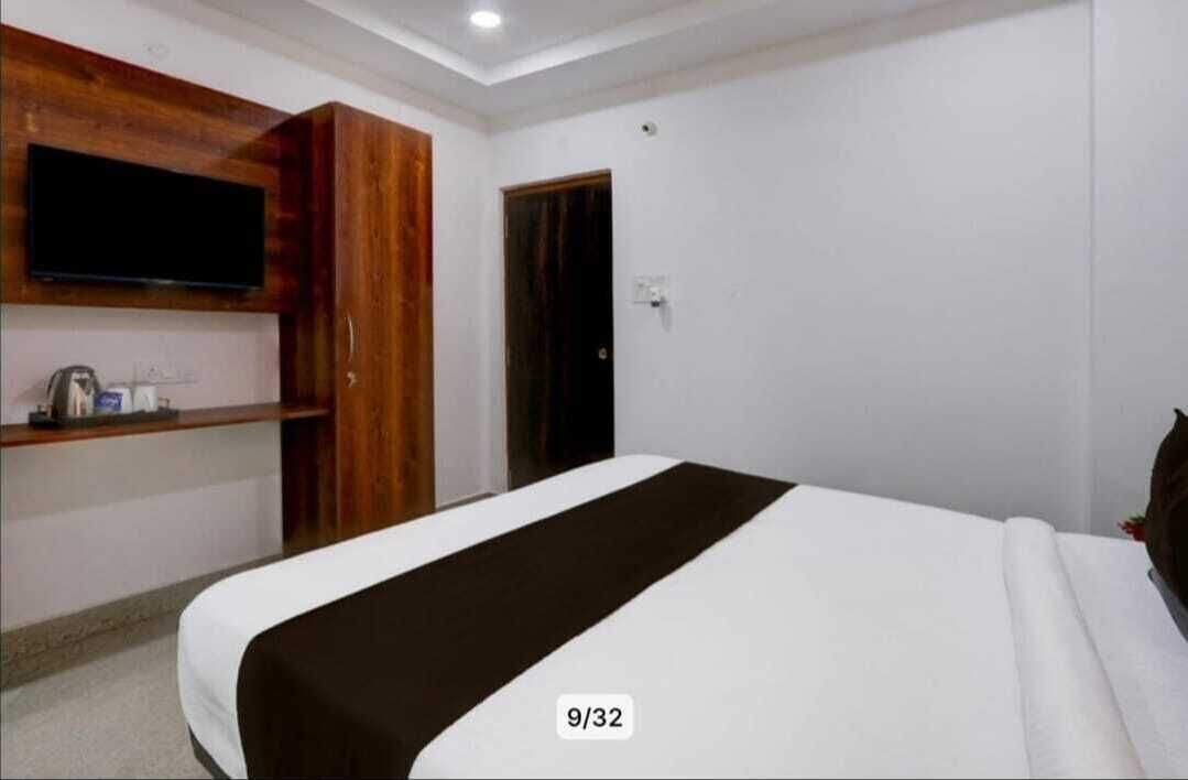 A hotel room with a bed, a TV mounted on the wall, a wooden cabinet, and a door.