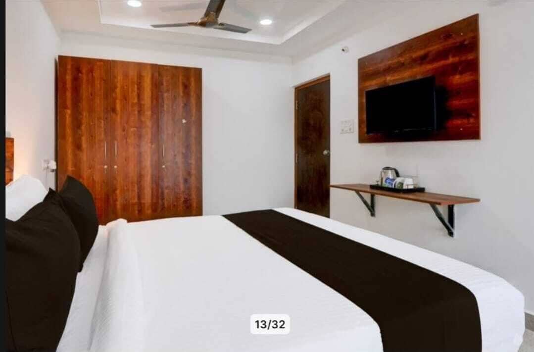 A bedroom with a bed, a wooden wardrobe, a mounted TV, and a small table.