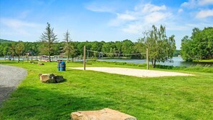 A volleyball court with a net, surrounded by a grassy area and trees, near a lake. - Sleeps 13 • Private Sauna • Hot Tub • Game Room (Pocono Lake)