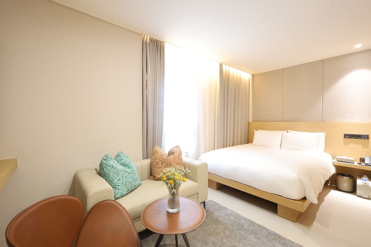 Et hotelværelse med seng, sofa, lille bord og en vase med blomster.