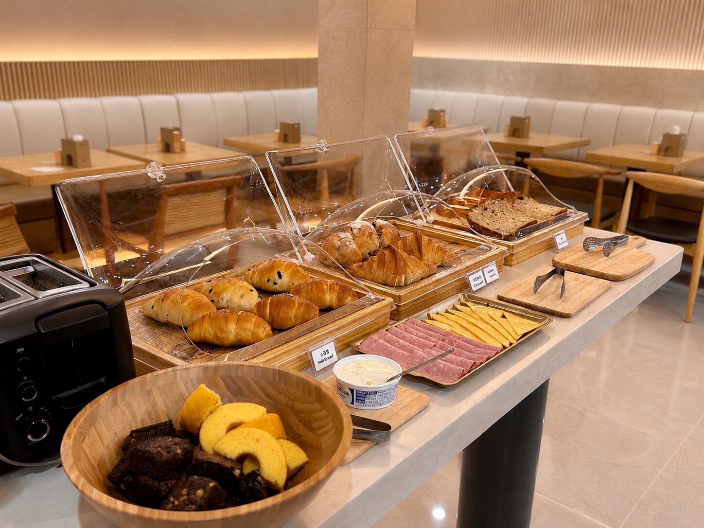 A breakfast buffet with various pastries, meats, and a bowl of fruit.