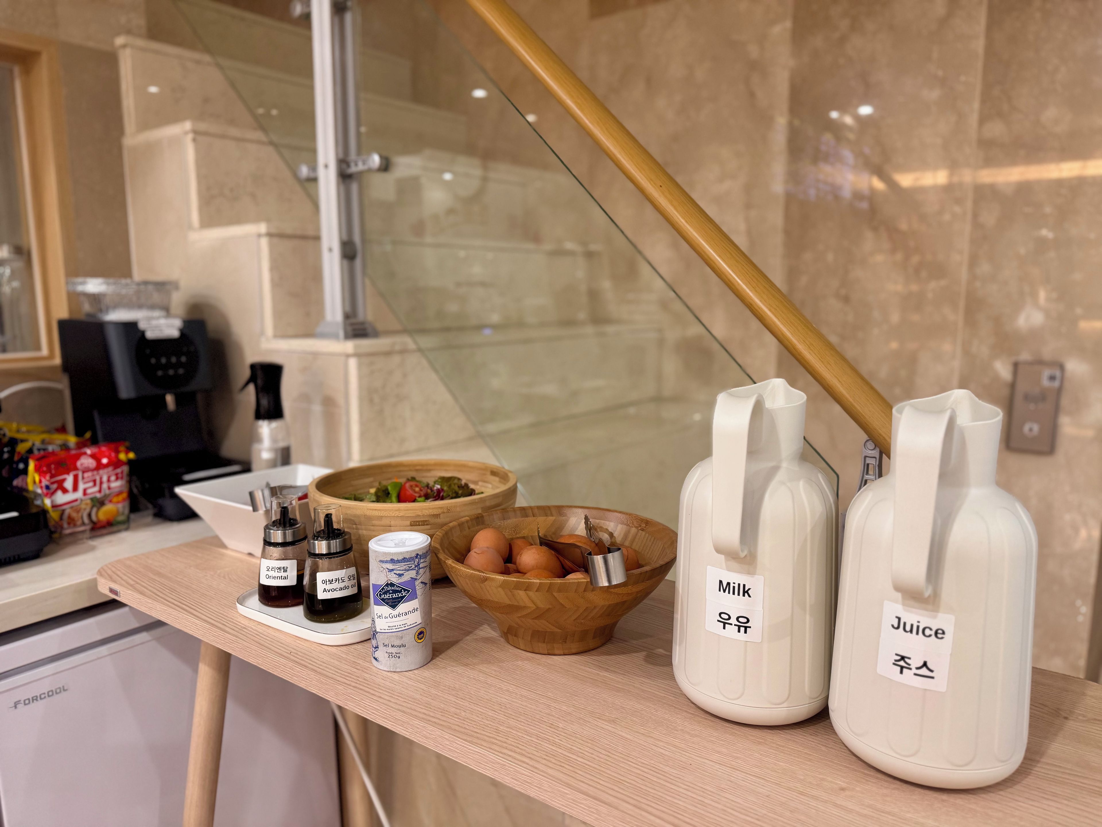 A kitchen counter with a coffee machine, a bowl of eggs, and bottles labeled 'Milk' and 'Juice'.