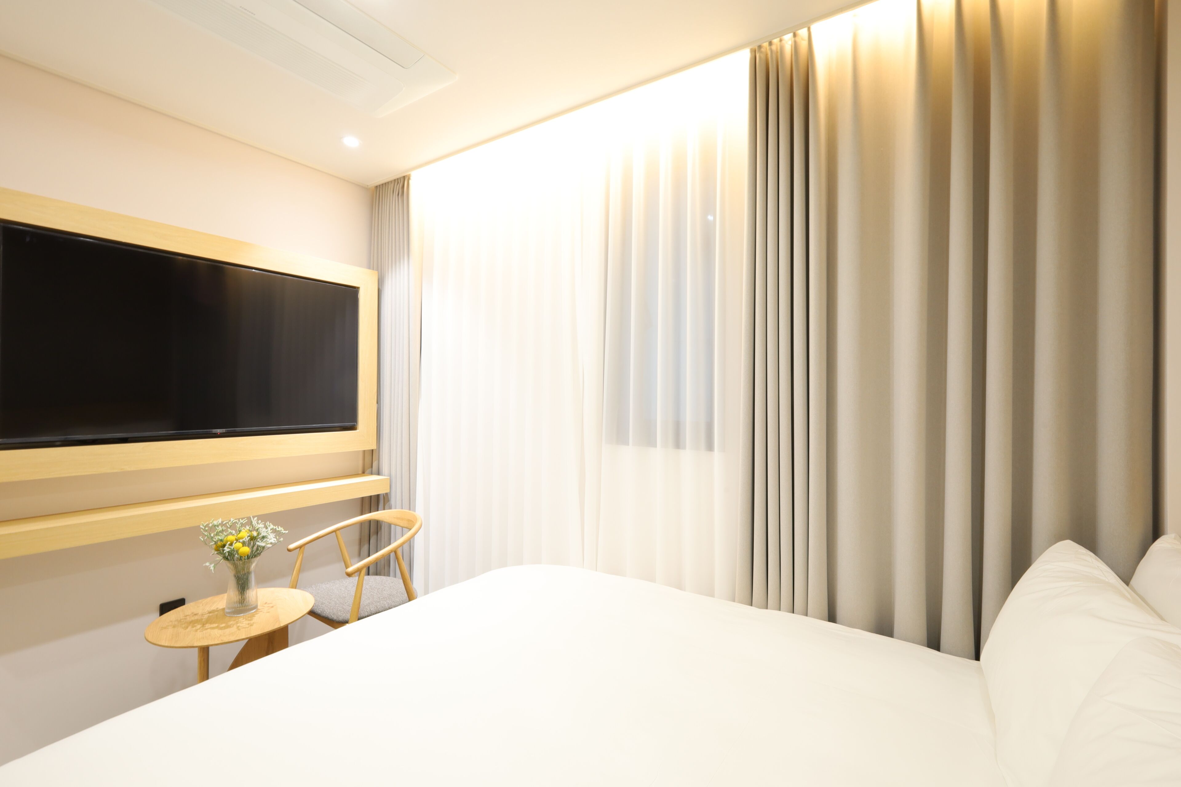 Una habitación de hotel con cama, televisión, una mesita redonda con un florero y una silla.