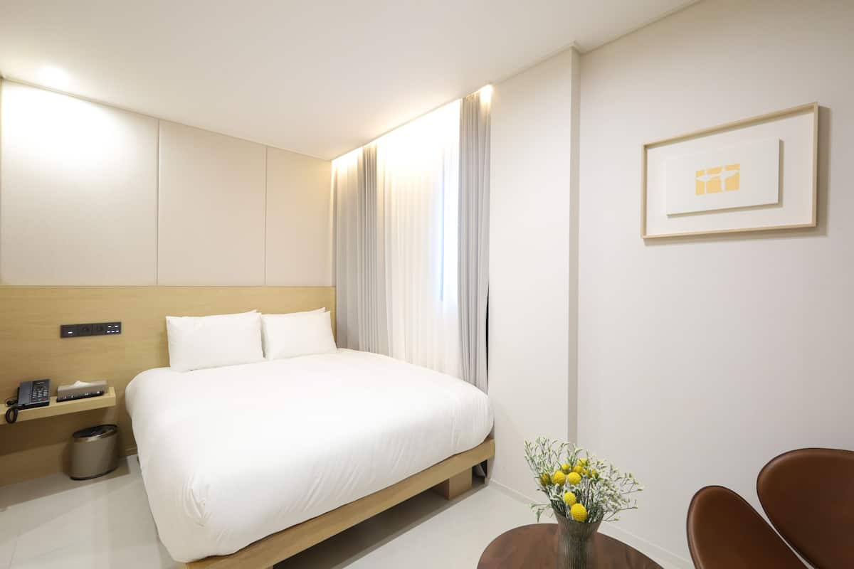 Et hotelværelse med seng, sengebord, lampe og et billede i ramme på væggen.