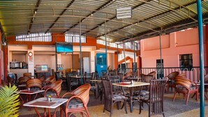 An outdoor cafe with multiple tables and wicker chairs, a covered seating area, and a visible kitchen in the background. - Latahzan guest house (Moyale)