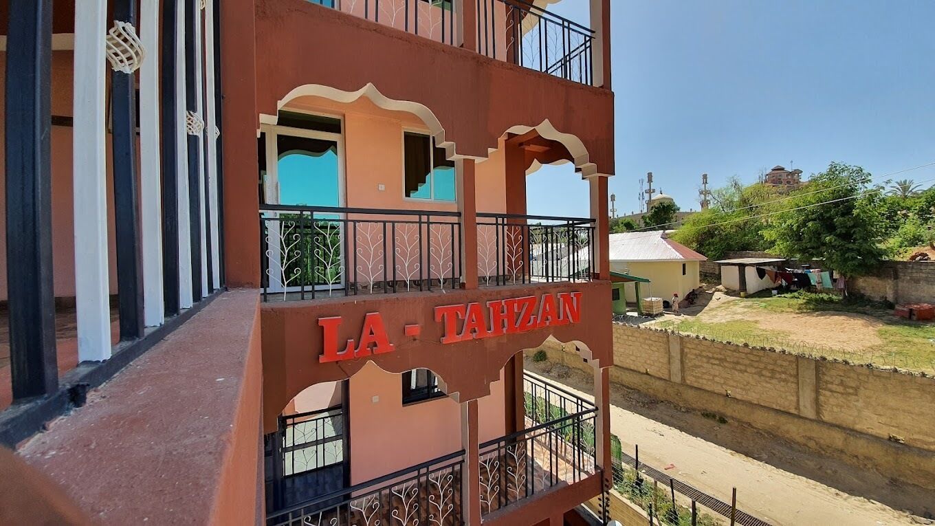 A multi-story building with balconies and a sign reading "LA TAHZAN".