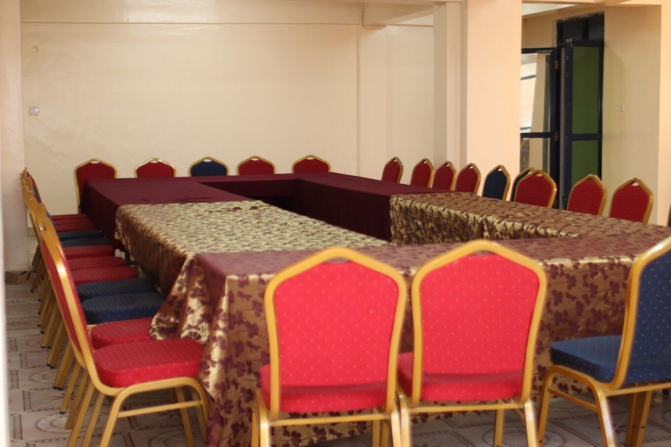 A conference room with a long table, red and blue chairs, and patterned tablecloths.