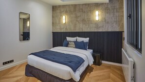 A modern bedroom with a skylight, a large bed with a blue and white duvet, a dark headboard, and two wall-mounted lights. - Superb & New Apartment Saint Germain des Près (Paris)