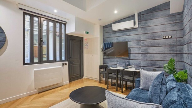 A modern hotel room with a dining area, a sofa, and a large window with blinds. - Superb & New Apartment Saint Germain des Près (Paris)