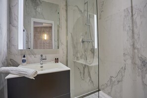 Un baño moderno con lavamanos de mármol, ducha con cerramiento de vidrio y un espejo grande.