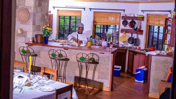A chef preparing food in a kitchen with a bar area, dining tables, and a view of the outdoors. - The Cottage is Situated on a Farm in Laikipia 32km From Nanyuki - 2330 (Ethi)